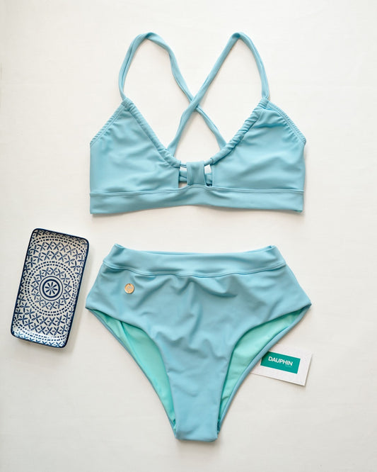 Light blue cross-back bikini top and high-waisted bottom set, presented next to a patterned phone case, capturing a relaxed beach vibe.