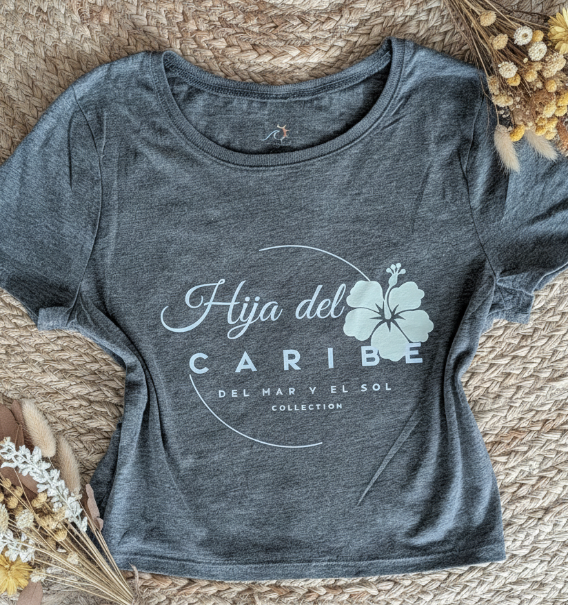 Gray t-shirt with 'Hija del Caribe' design on a woven surface with dried flowers.