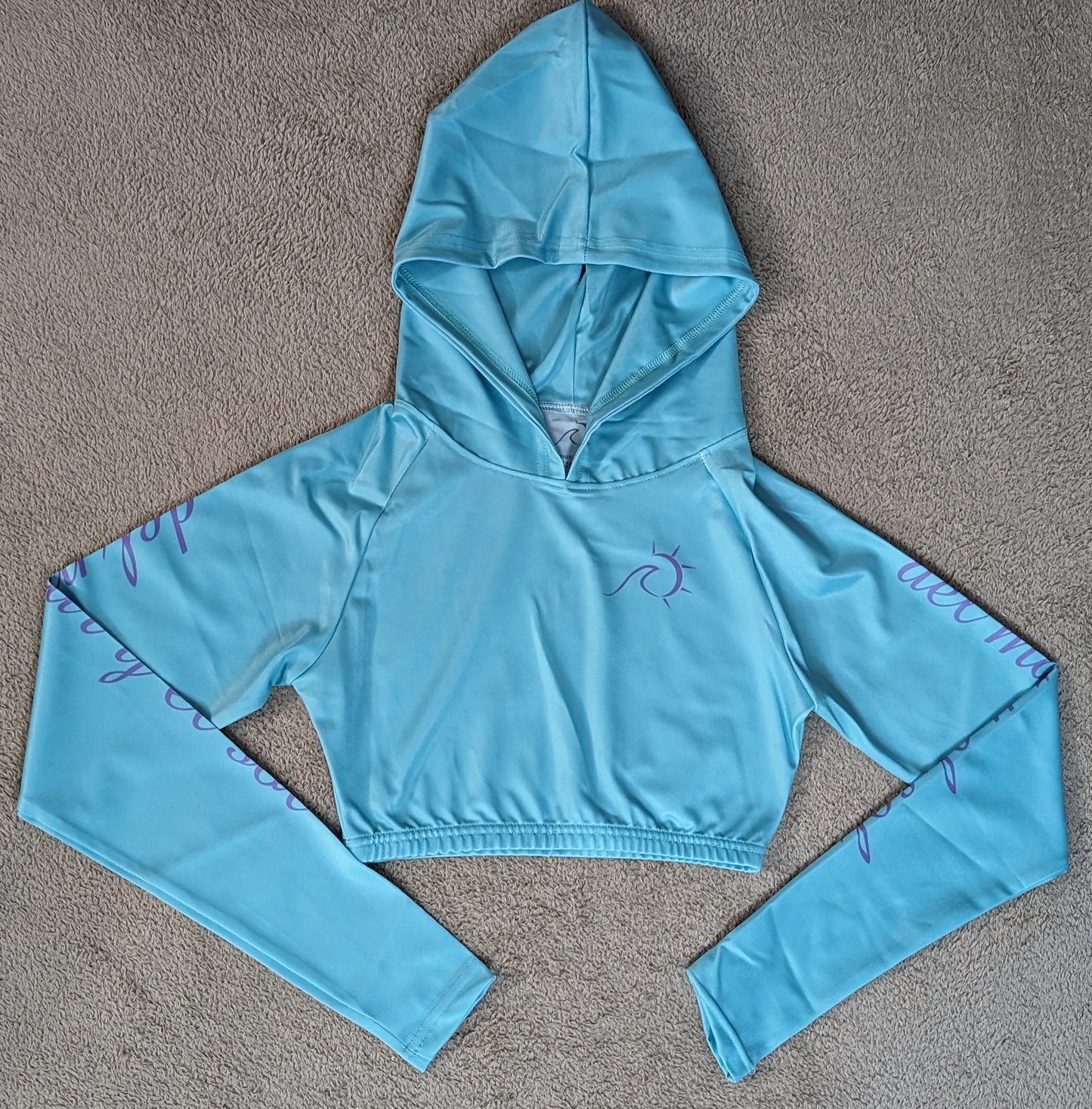 Sky blue cropped rash guard with purple script accents on the sleeves.