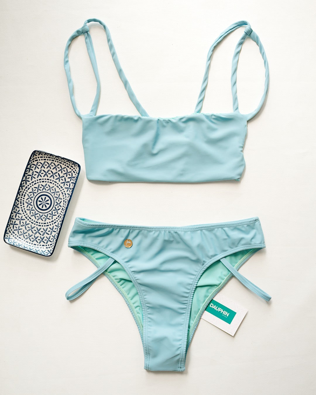 Sky blue Palm bikini top with a tie-back feature and Tobago bottoms with strappy side details, presented with a phone case for a complete summer look.