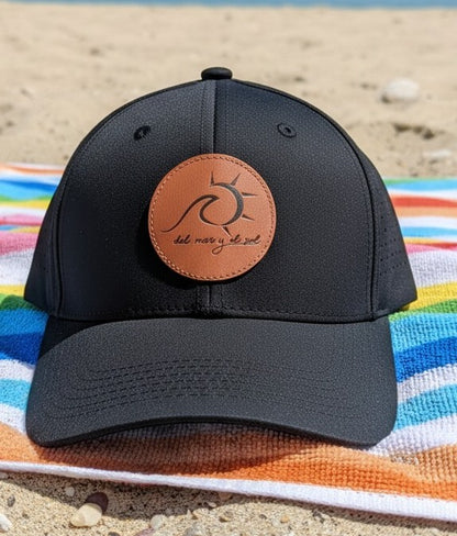 Black cap with a brown leather patch on a colorful towel at the beach