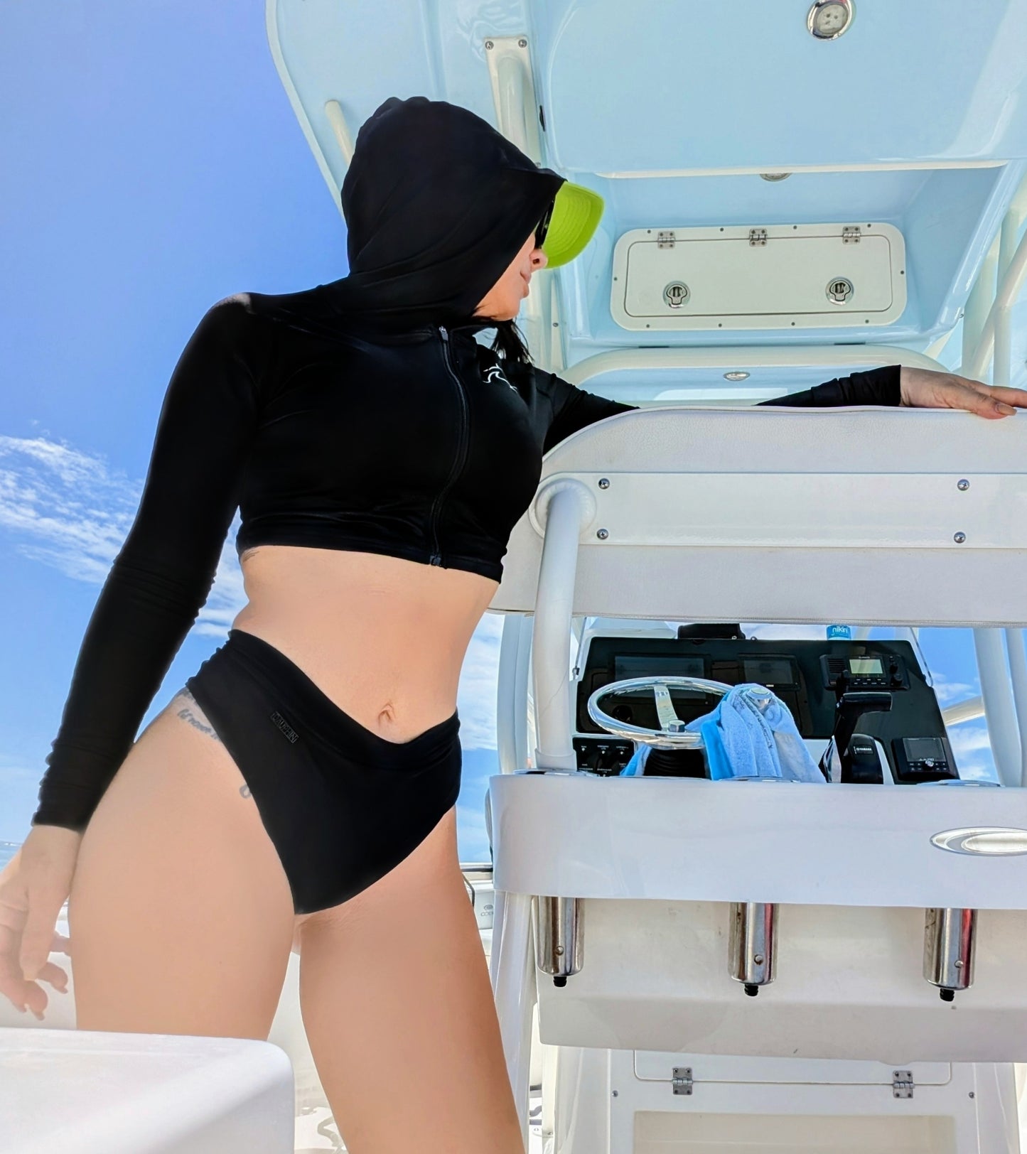 Person wearing a black swimsuit and hood crop rashguard on a boat