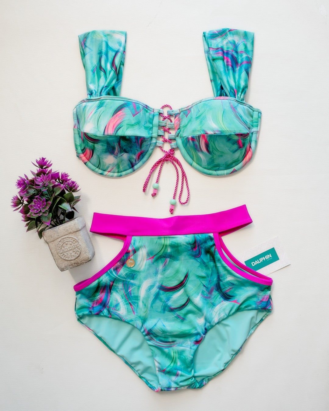 Belice tie-back bikini top with turquoise and pink swirls, matched with Tropical Reef high-waist bottoms with a bright pink band, showcased with a potted plant.