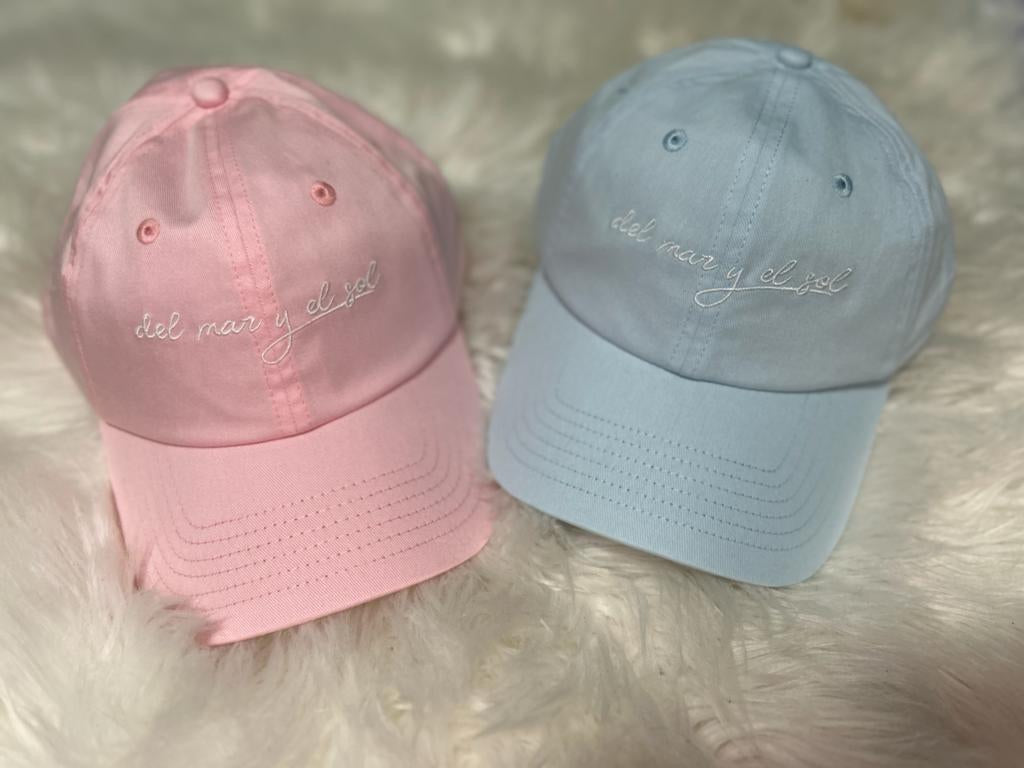 Two baseball caps, one pink and one blue, with embroidered text on the front.