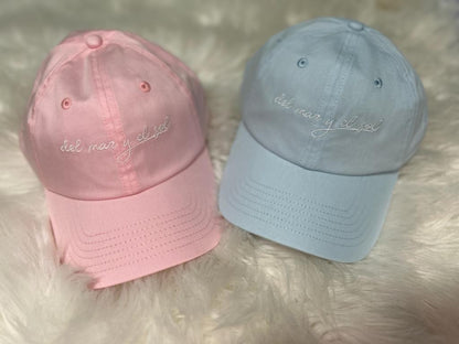 Two baseball caps, one pink and one blue, with embroidered text on the front.