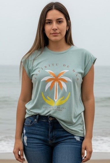 Woman wearing a light green t-shirt with a palm tree design on a beach.