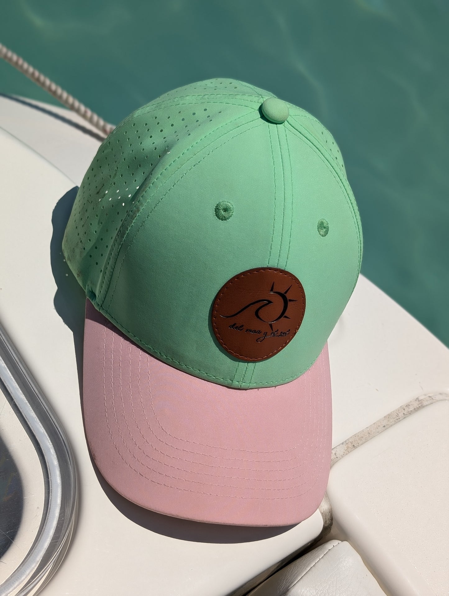 Island Mint and Beige dry fit cap resting on a boat by the sea. 
