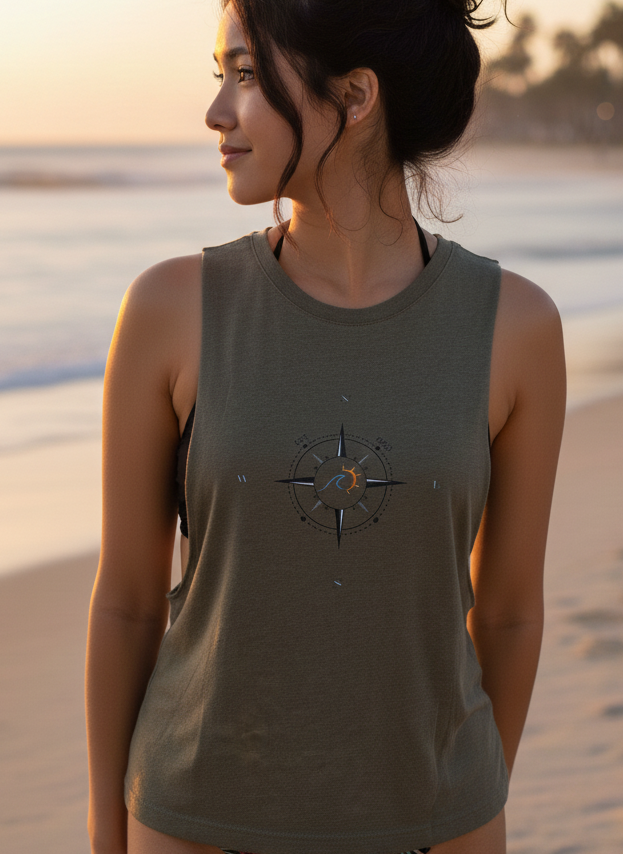 Woman wearing a sleeveless shirt with a compass design on a beach at sunset.