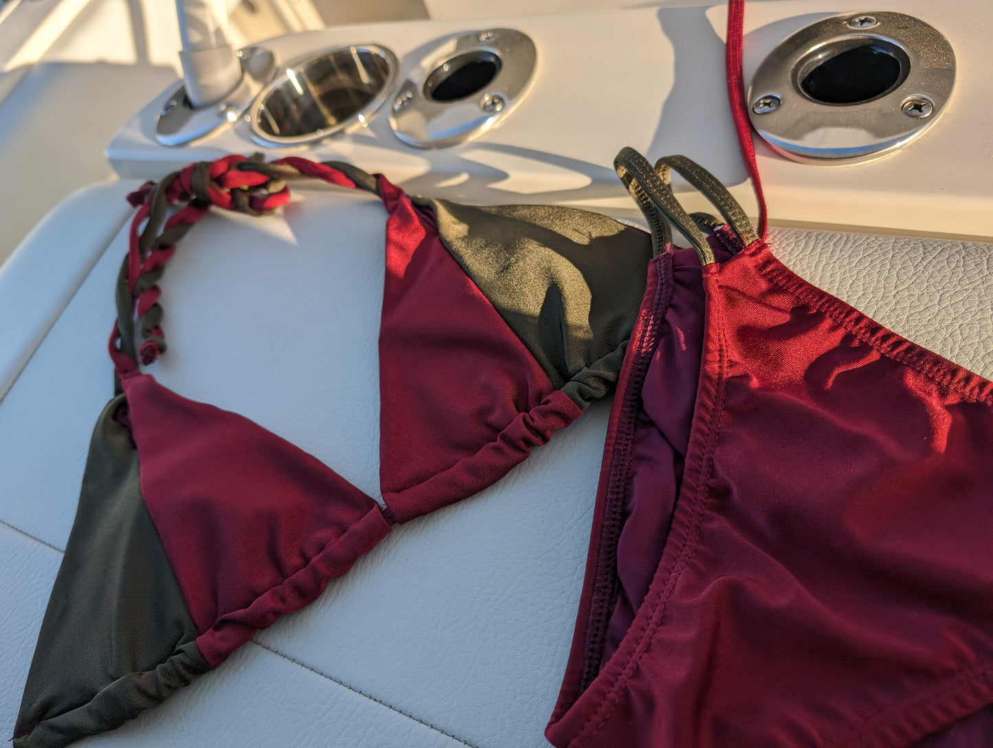 Full view of maroon and olive two-piece swimsuit set on a boat deck.