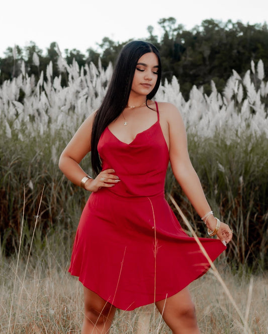 Woman wearing a wine red short dress with adjustable straps and a soft feminine silhouette in a coastal setting